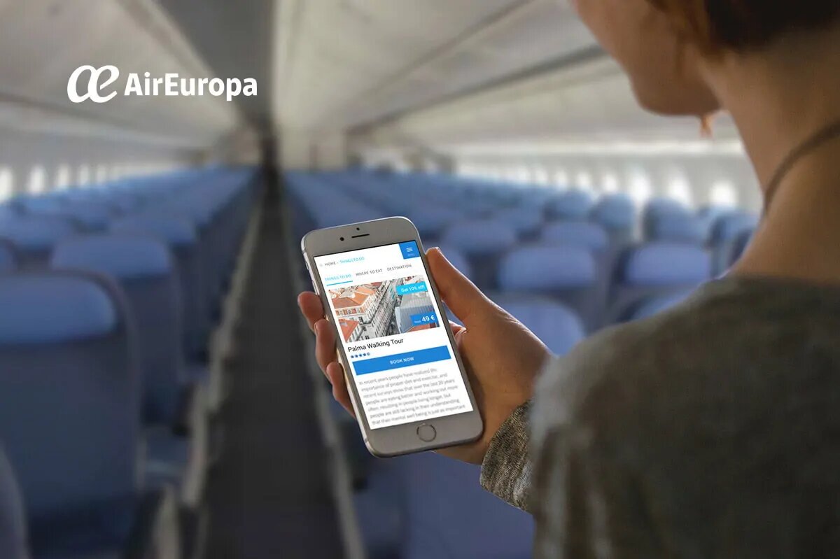 A person holding an iPhone inside the aircraft with the in-flight portal open - reading about the destination walking tour. A realistic mockup.